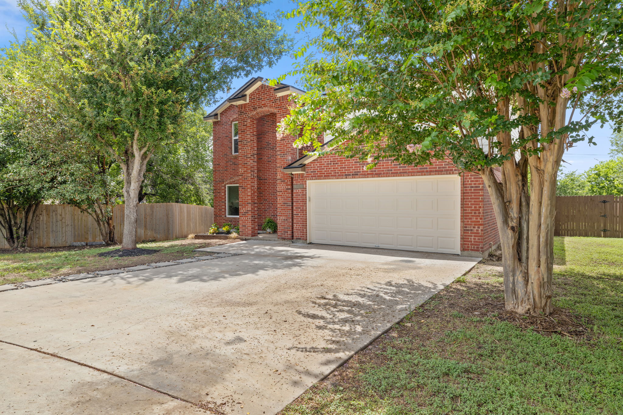 909 Rocking Spur Cove Pflugerville, TX 78660 - Photo 3 of 33 A well-maintained brick exterior home featuring a two-car garage and concrete driveway amidst lush trees.