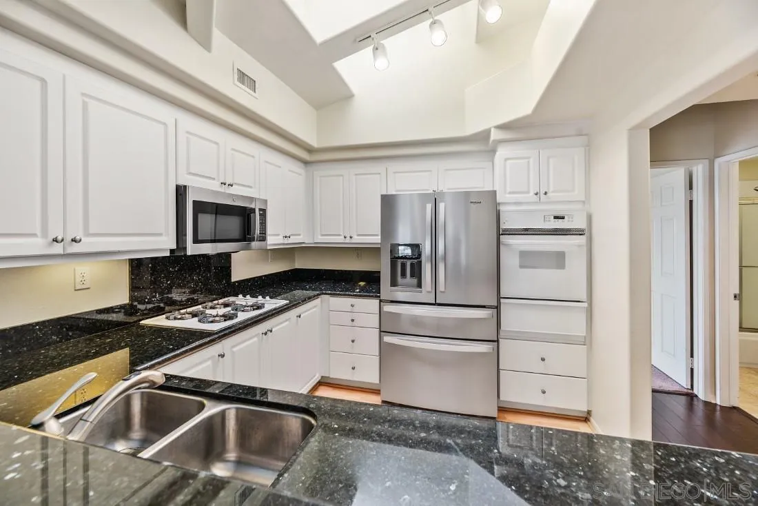 8637 Via Mallorca, Unit E La Jolla, CA 92037 - Photo 8 of 34 a kitchen with granite countertop a refrigerator sink and white cabinets