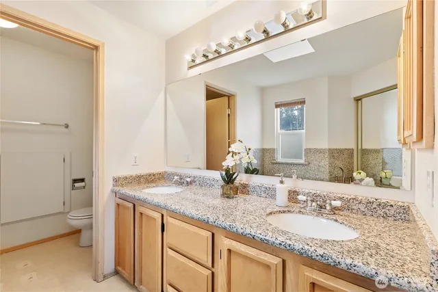 a bathroom with a granite countertop double vanity sink mirror and toilet