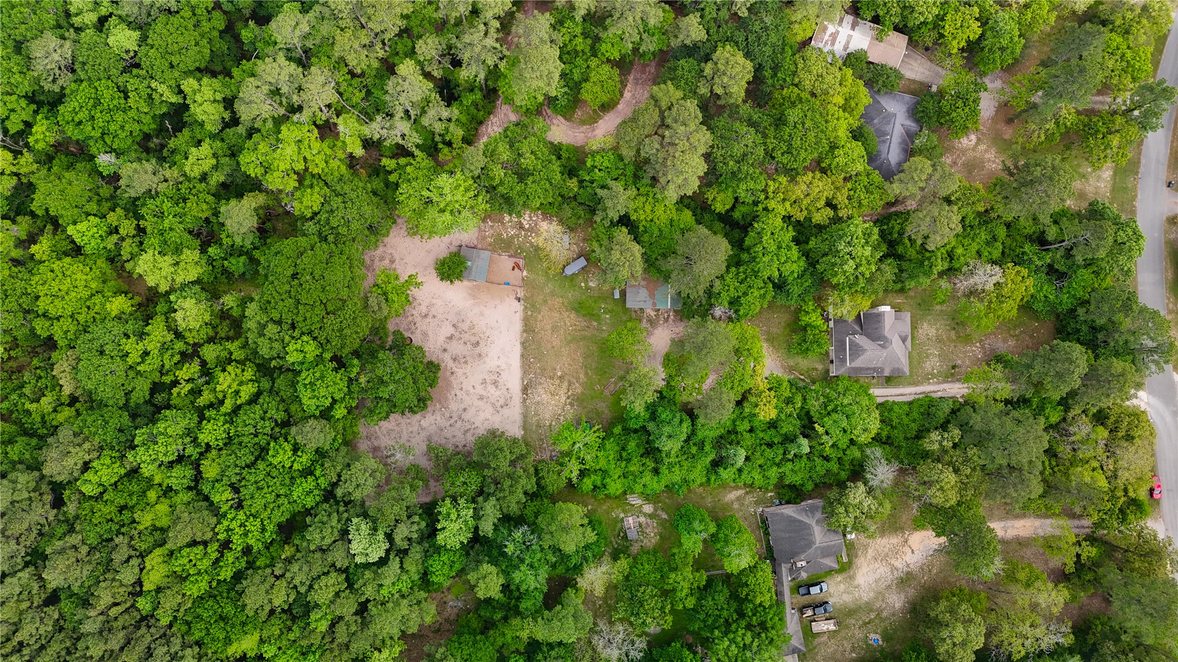25903 Penguin Street Magnolia, TX 77355 - Photo 9 of 46 This aerial photo showcases a wooded area with a few scattered homes nestled among dense greenery. The properties are surrounded by trees, offering privacy and a natural setting. A visible road provides access to the homes, suggesting a serene, secluded neighborhood ideal for nature lovers.