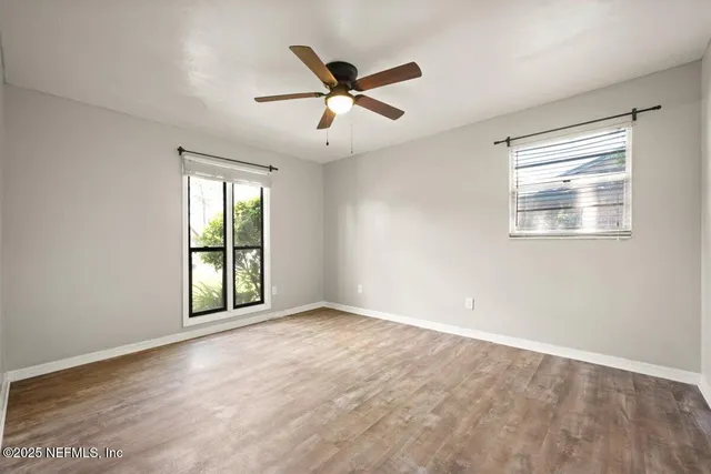 an empty room with wooden floor ceiling fan and windows