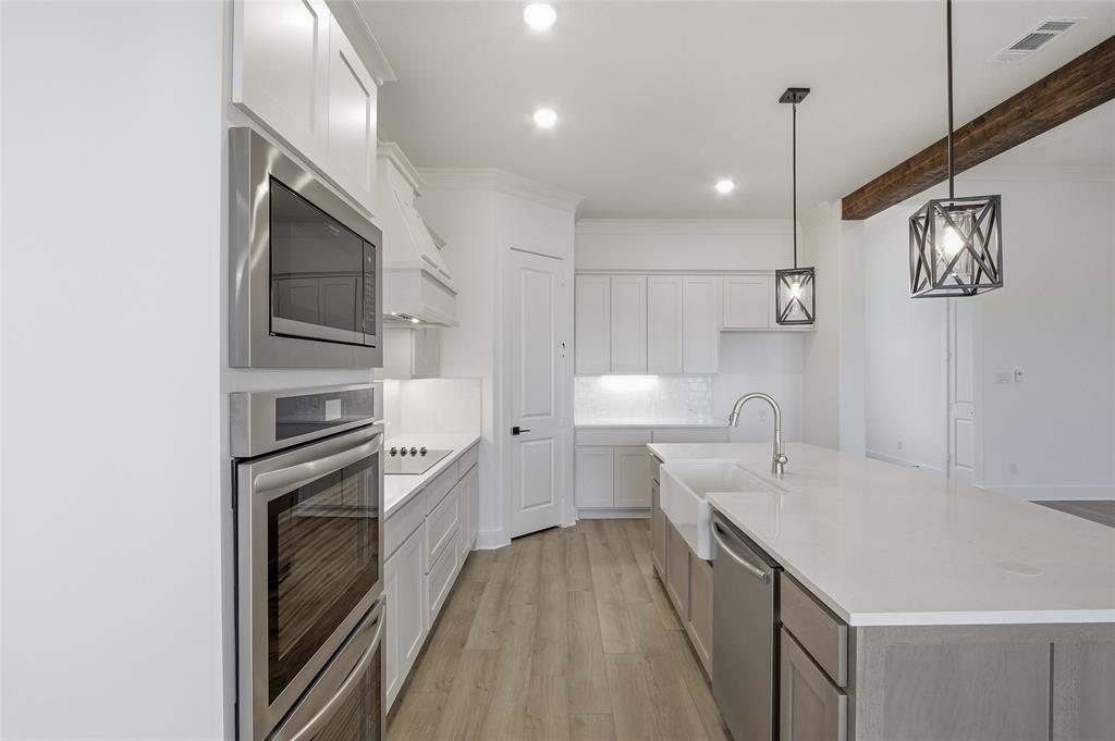 810 Vly Rdg Road Van Alstyne, TX 75495 - Photo 12 of 39 Dual tone kitchen featuring stainless steel appliances, light wood-style flooring, a kitchen island with sink, light stone countertops, and decorative light fixtures