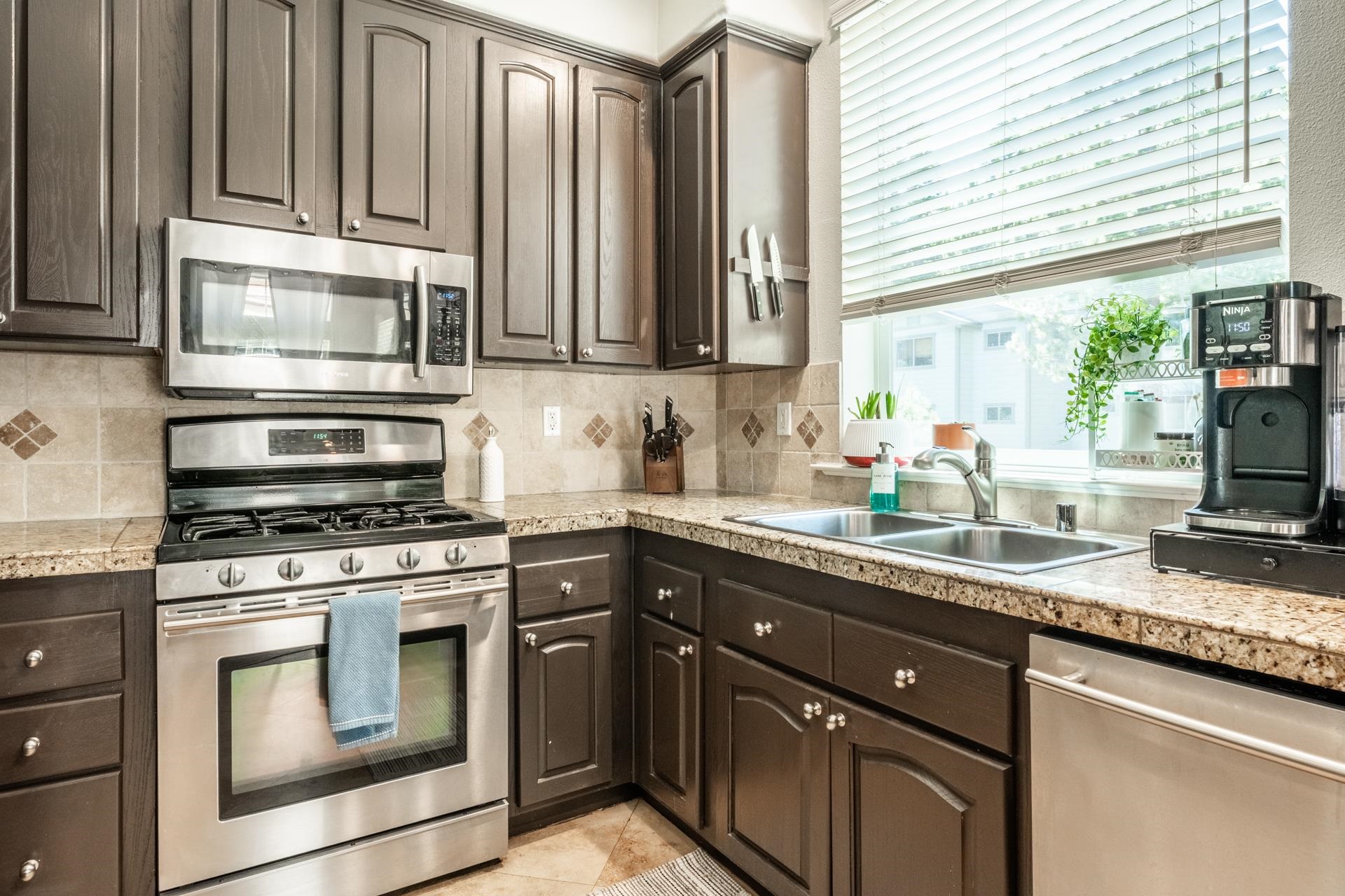 1787 Old Mammoth Road, Unit 2 Mammoth Lakes, CA 93546 - Photo 9 of 29 Kitchen featuring dark wood cabinetry, stainless steel appliances, light-toned countertops, tile backsplash, and a double basin sink