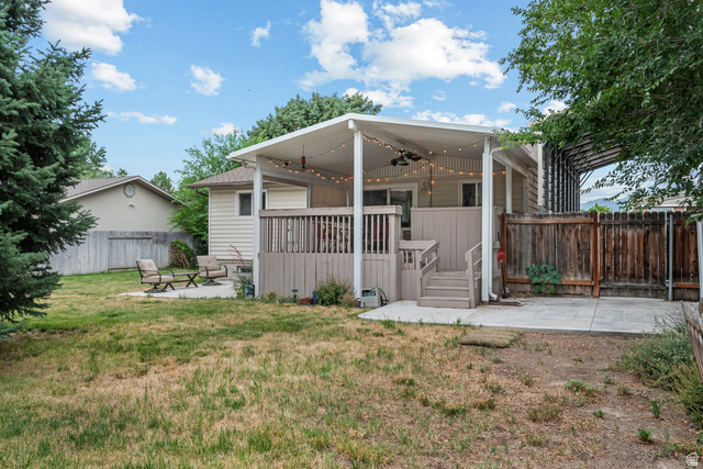 7659 State Street Midvale, UT 84047 - Photo 28 of 33 Spacious backyard featuring a covered deck, wood fence, mature evergreen tree, and concrete patio