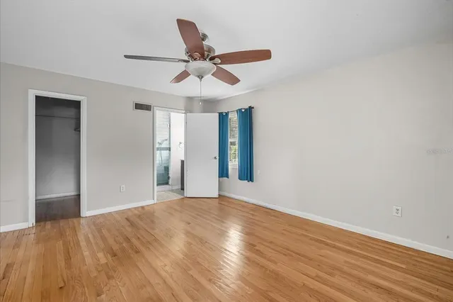a view of an empty room with wooden floor and a ceiling fan