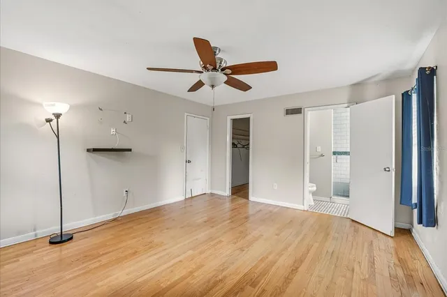 a view of an empty room with wooden floor and a ceiling fan
