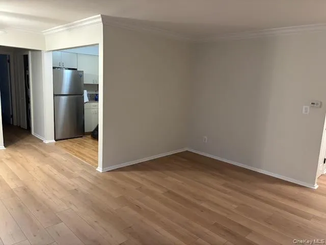a view of an empty room with wooden floor and a kitchen