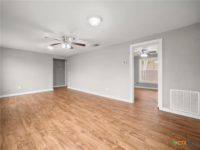 a view of an empty room with wooden floor and a ceiling fan