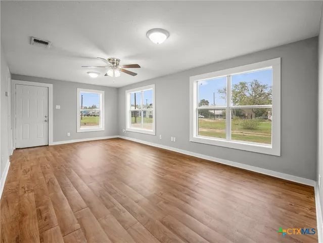 a view of an empty room with wooden floor and a window