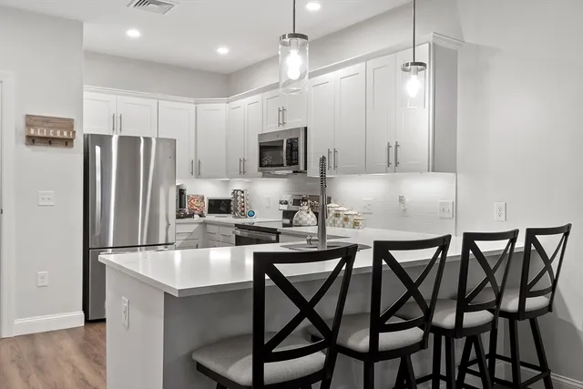 a kitchen with stainless steel appliances granite countertop a dining table chairs refrigerator and microwave