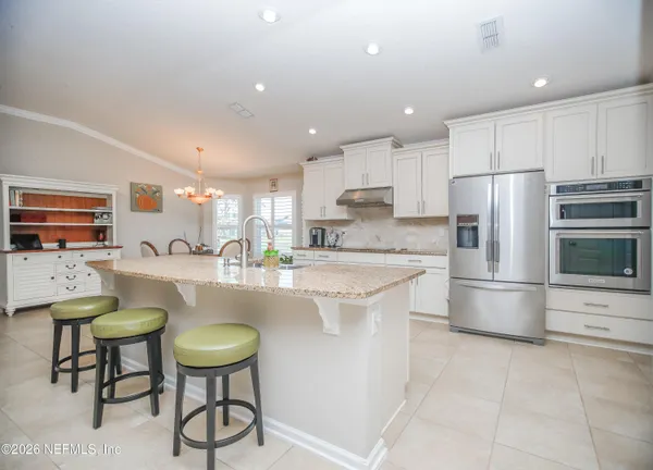 a kitchen with stainless steel appliances granite countertop a sink a stove a refrigerator cabinets and chairs