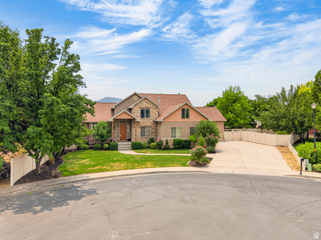 1279 West 1500th Street North Mapleton, UT 84664 - Photo 71 of 83 Stone and stucco exterior featuring a prominent front entrance with a wood door, an attached concrete driveway, a manicured lawn, mature trees, and a mountain backdrop