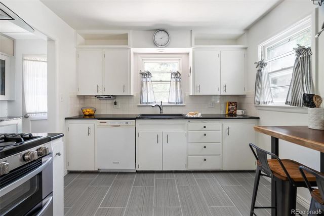 a kitchen with granite countertop white cabinets appliances and a window