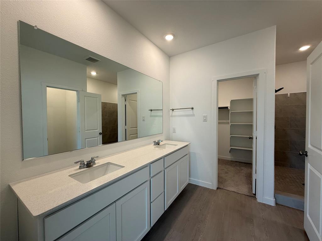 3025 Timber Rdg Drive Anna, TX 75409 - Photo 18 of 23 Dual vanity with light-toned countertop and integrated sinks, wood-finish flooring, and built-in shelving in an adjacent space