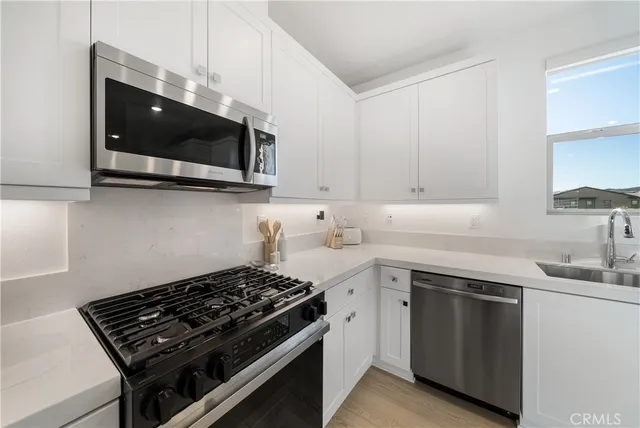 a kitchen with stainless steel appliances a sink dishwasher a stove microwave and oven with white cabinets