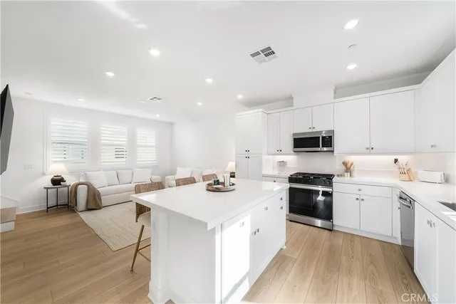 a kitchen with stainless steel appliances a stove a sink a stove a refrigerator and white cabinets with wooden floor