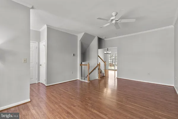 a view of an empty room with wooden floor and a ceiling fan