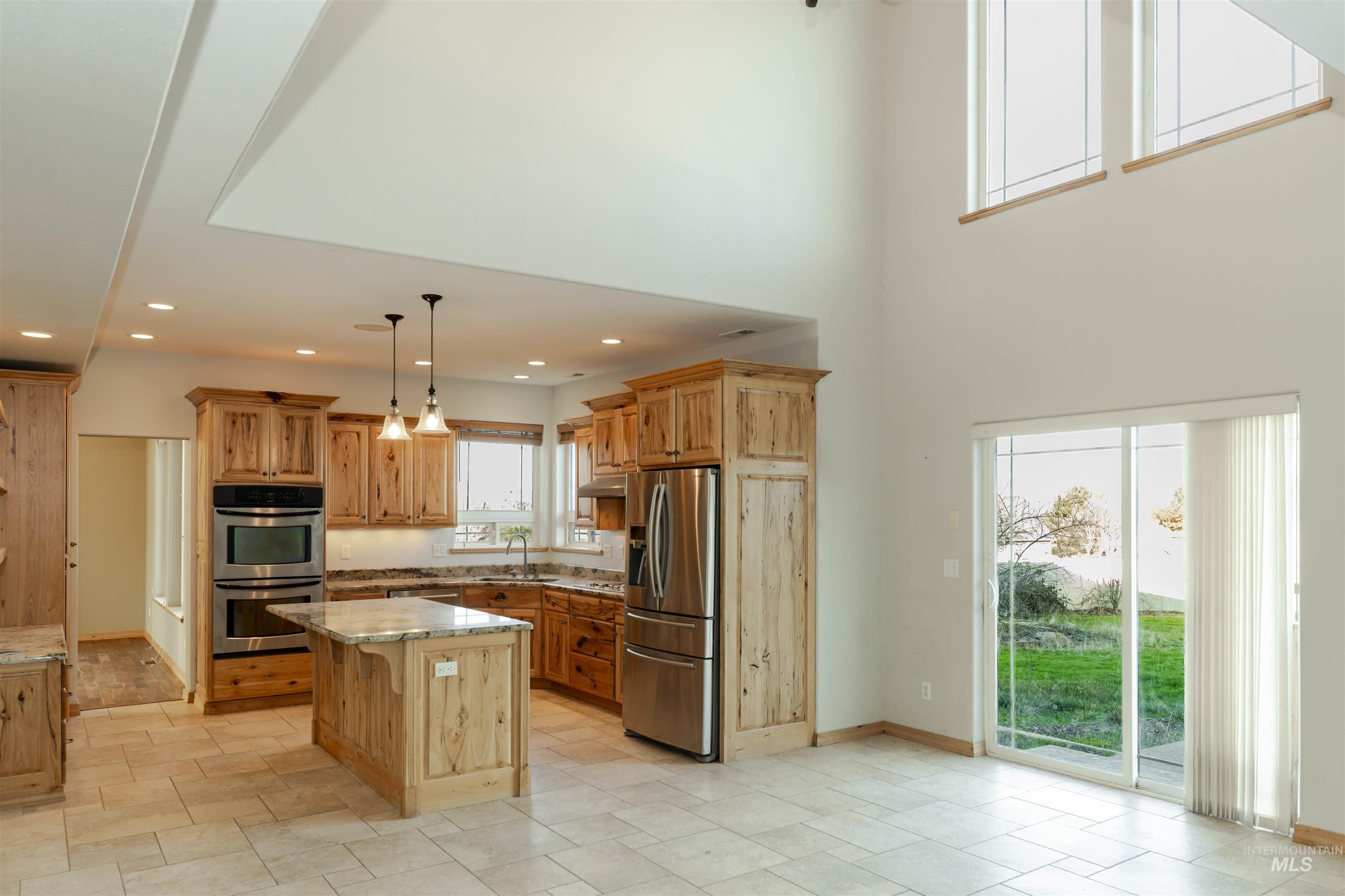 7591 Pheasant Chase Drive Lewiston, ID 83501 - Photo 10 of 32 Kitchen with appliances with stainless steel finishes, light stone counters, a kitchen island, decorative light fixtures, and a towering ceiling