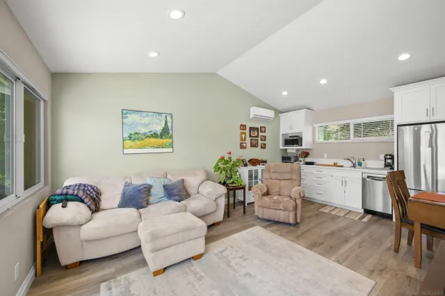 a living room with kitchen island furniture a refrigerator and a dining table with wooden floor