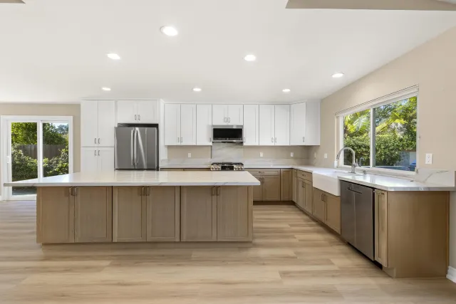 a large kitchen with stainless steel appliances a large counter top a stove a refrigerator cabinets and a window