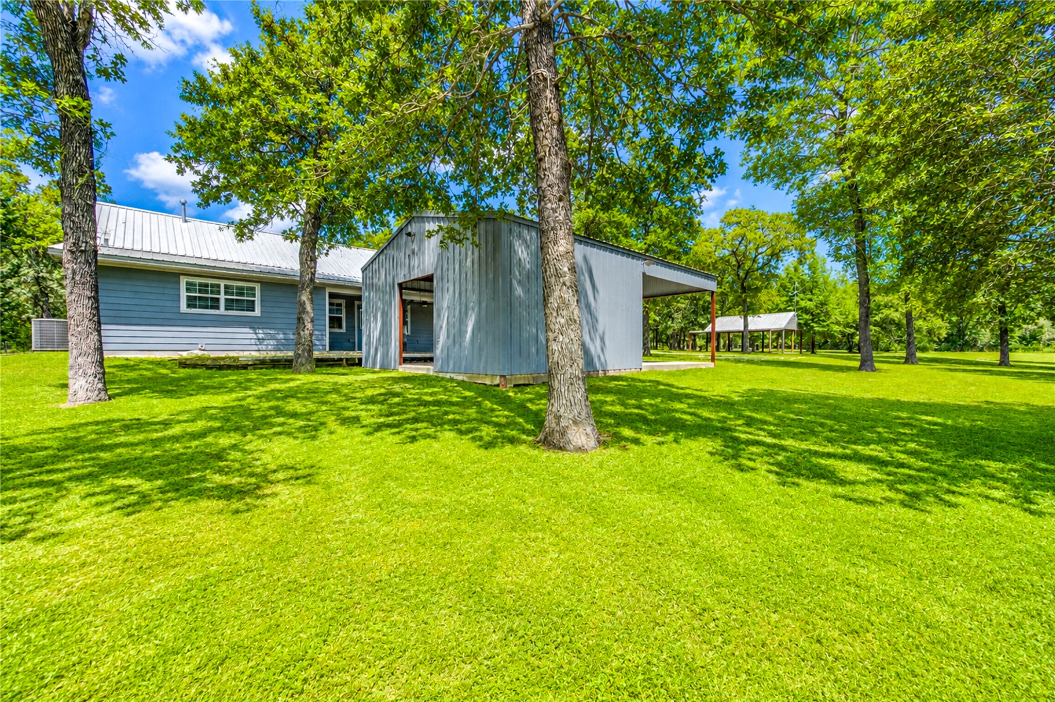 8805 Sun Oil Road Brenham, TX 77833 - Photo 4 of 50 Charming home with a spacious yard surrounded by mature trees, featuring a metal roof and a detached structure perfect for storage or a workshop.