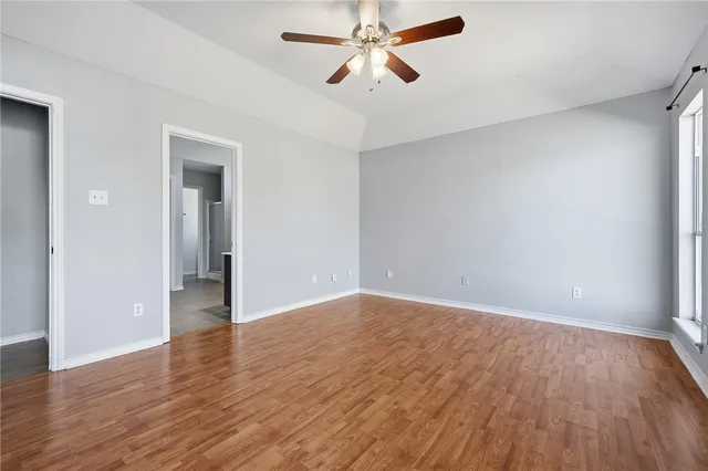 an empty room with wooden floor ceiling fan and windows