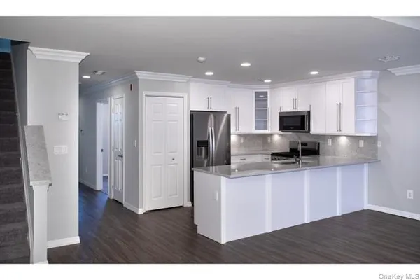 a kitchen with stainless steel appliances granite countertop a refrigerator a sink a stove a microwave and white cabinets with wooden floors