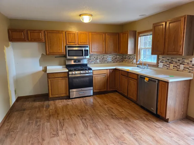 a kitchen with stainless steel appliances granite countertop a stove a sink dishwasher and a microwave oven on the wooden floor
