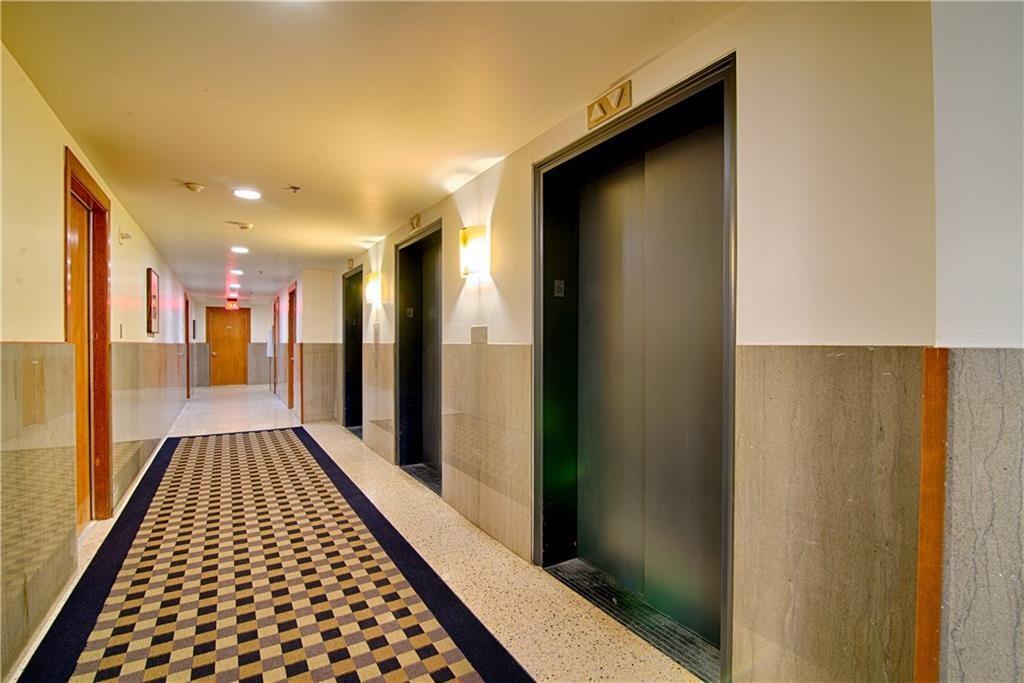 710 Colorado Street, Unit G9 Austin, TX 78701 - Photo 22 of 25 A long, illuminated hallway with stylish wall sconces and multiple elevator entrances.