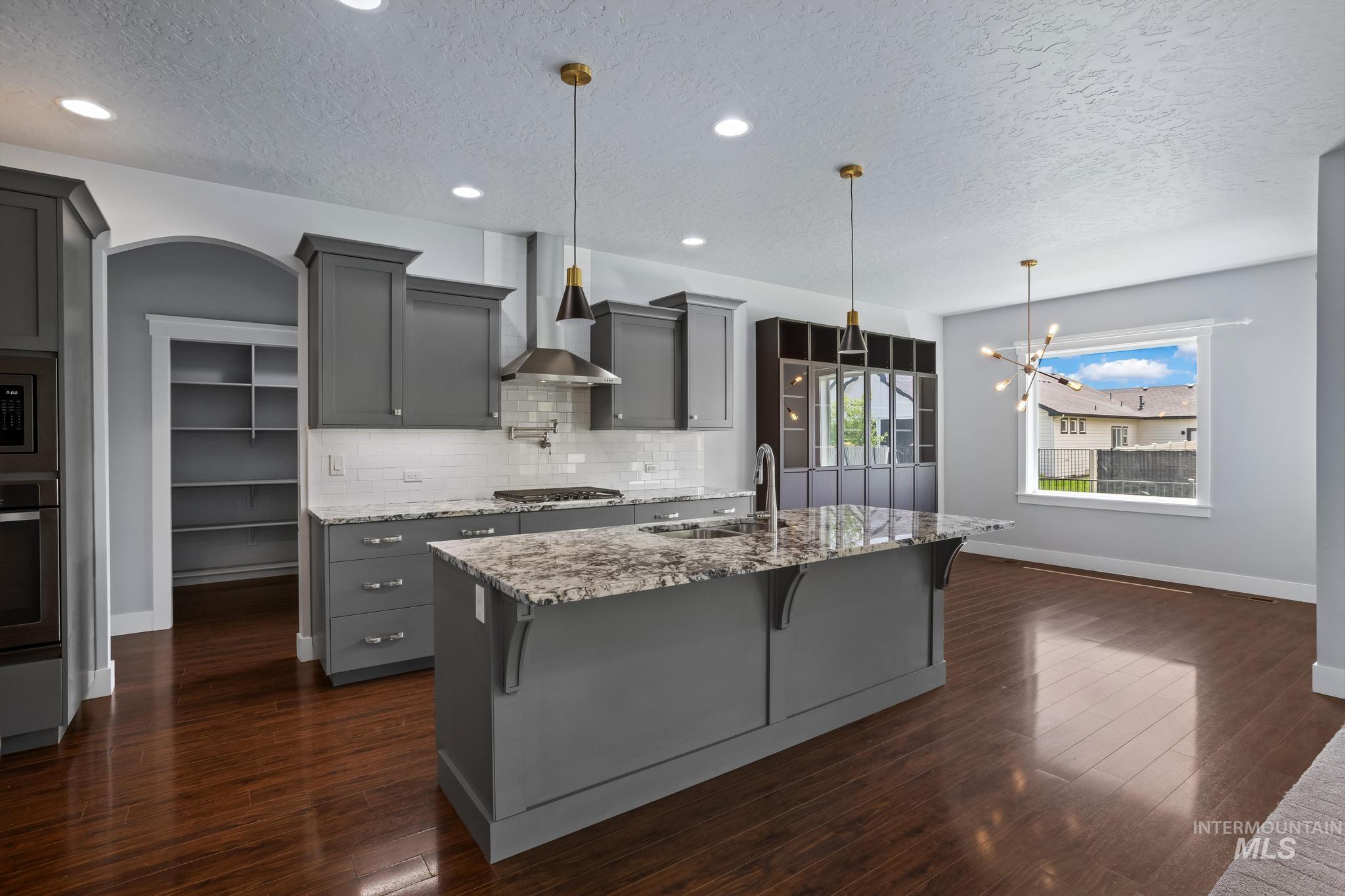 2681 East Rhyolite Court Nampa, ID 83686 - Photo 9 of 48 Contemporary kitchen featuring gray shaker-style cabinetry, a central island with a sink and pendant lighting, stainless steel appliances, and wood-finish flooring