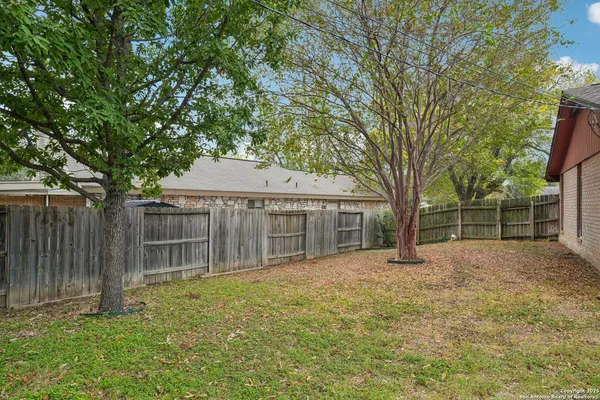 a backyard of a house with large trees and wooden fence