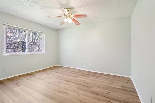 an empty room with wooden floor chandelier fan and windows