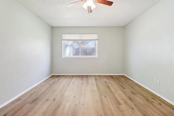 an empty room with wooden floor chandelier fan and windows