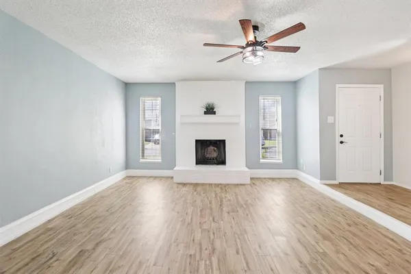 an empty room with wooden floor a ceiling fan a fireplace and windows