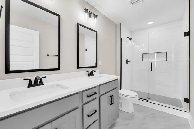 a bathroom with a double vanity sink toilet mirror and shower
