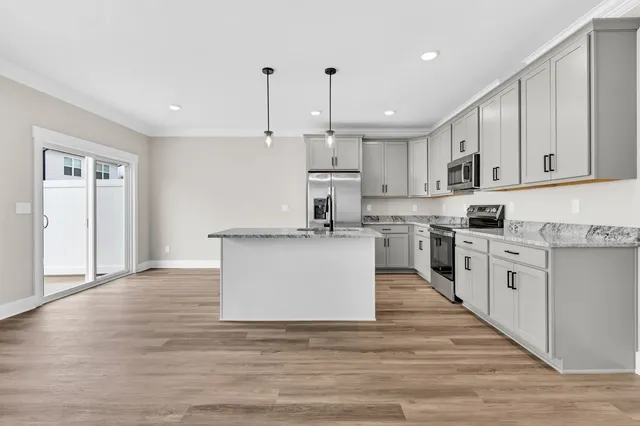 a large kitchen with stainless steel appliances kitchen island granite countertop a stove a sink a refrigerator and white cabinets with wooden floor