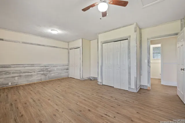 an empty room with wooden floor chandelier fan and windows