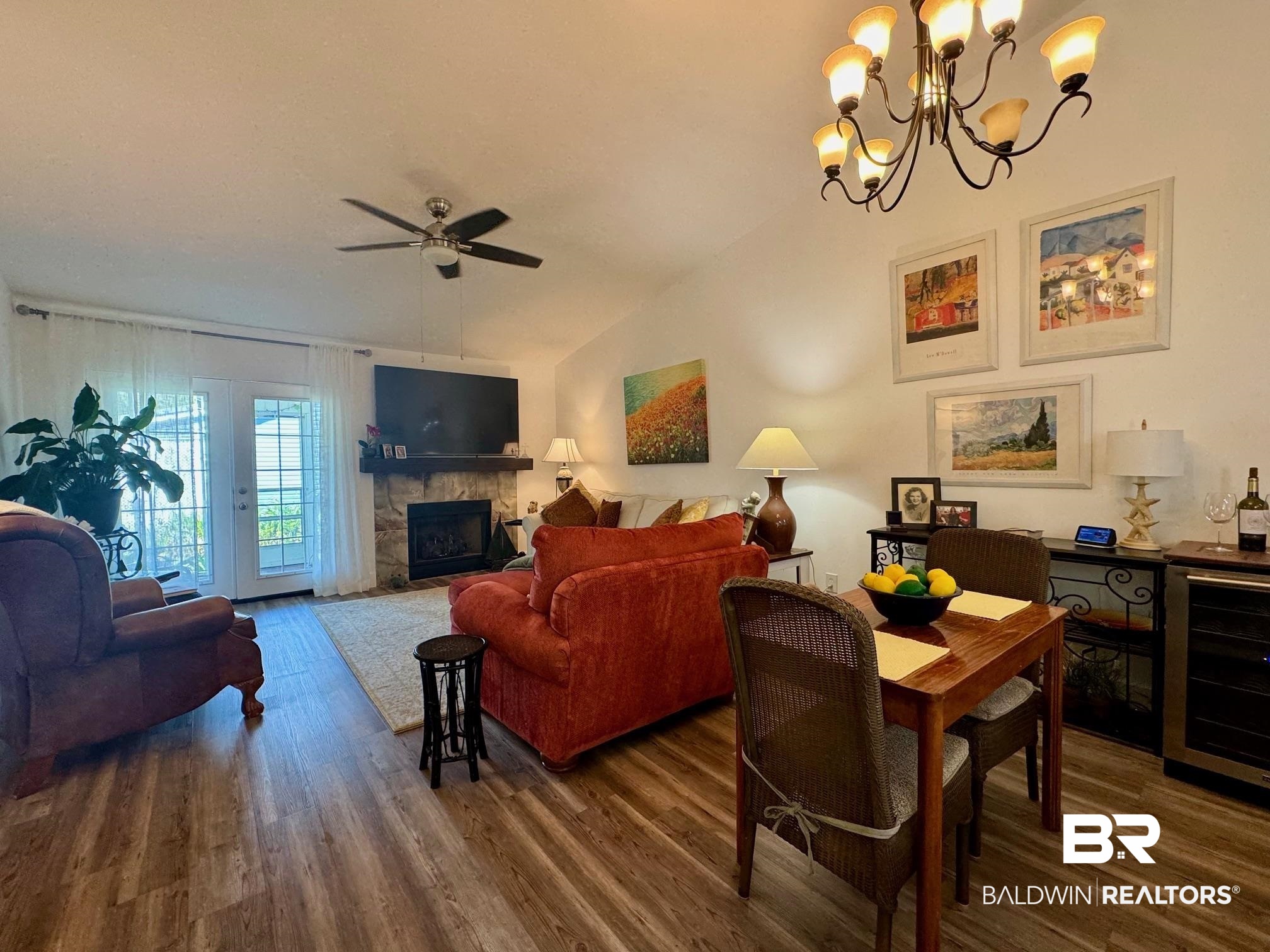 3200 Loop Road, Unit 55 Orange Beach, AL 36561 - Photo 5 of 40 Living room featuring lofted ceiling, a stone fireplace, beverage cooler, dark wood-type flooring, and ceiling fan with notable chandelier