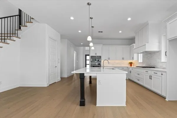 a kitchen with stainless steel appliances kitchen island granite countertop a stove top oven a sink a refrigerator and white cabinets with wooden floor