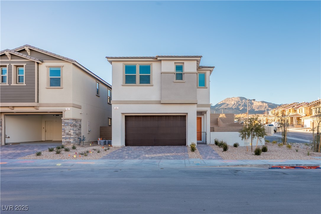 View of front facade with stucco siding, decorative driveway, an attached garage, and stone siding