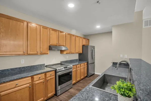 a kitchen with stainless steel appliances granite countertop a refrigerator a stove and a sink with wooden cabinets