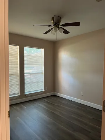 an empty room with wooden floor fan and windows
