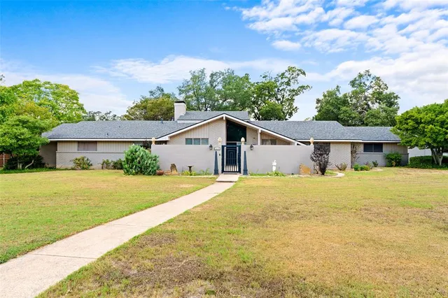a yellow house with a big yard plants and large trees