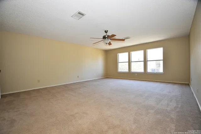 an empty room with chandelier fan and windows