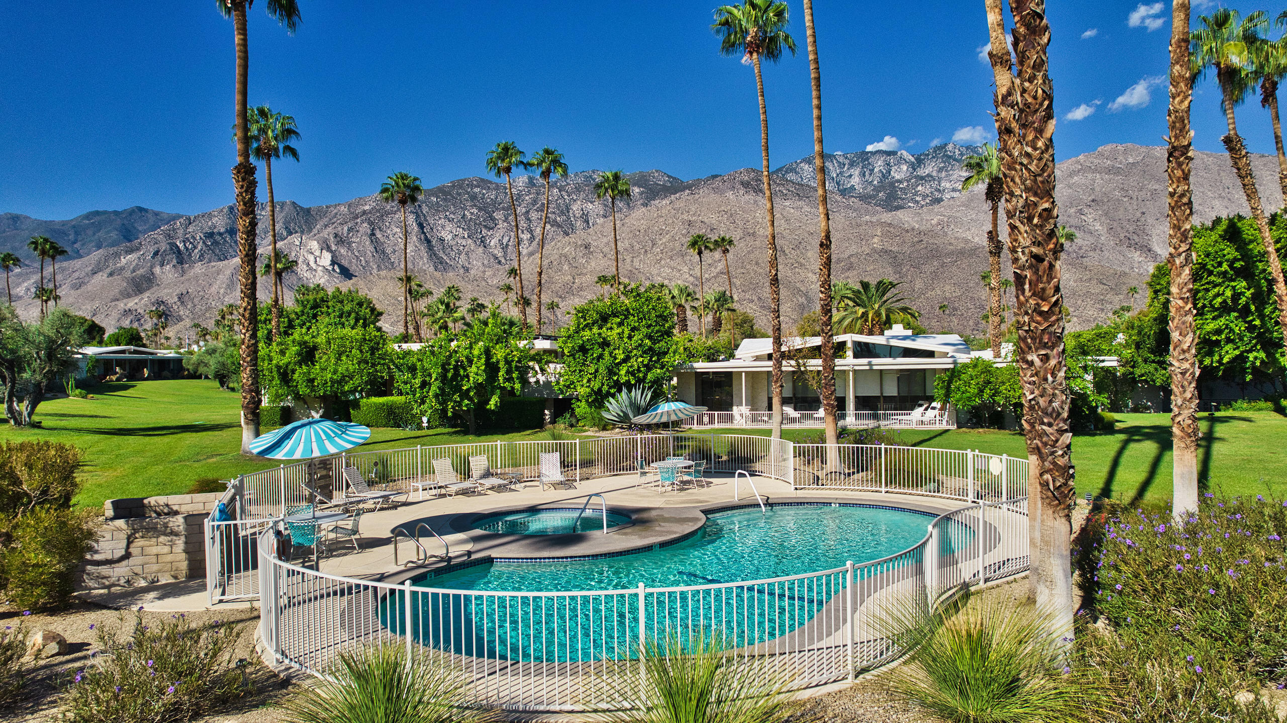 1570 South La Verne Way Palm Springs, CA 92264 - Photo 6 of 27 a view of a patio with couches table and chairs under an umbrella with a fire pit and wooden fence