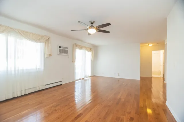 an empty room with wooden floor a ceiling fan and windows