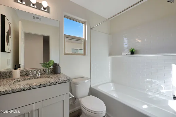 a bathroom with a granite countertop sink a toilet a mirror and bathtub