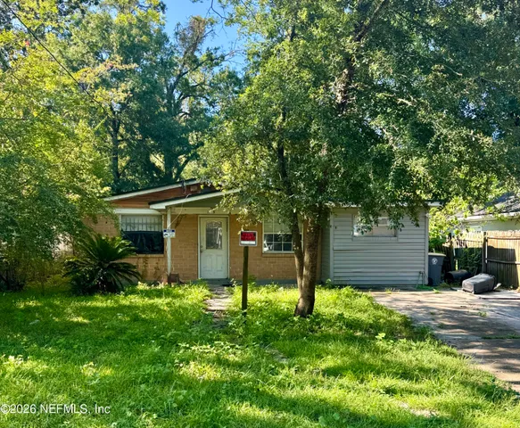 a view of a yard in front of a house with plants and large tree