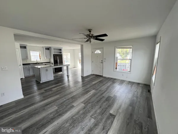 an empty room with wooden floor a ceiling fan and windows
