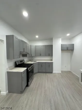a large kitchen with a stove a sink a refrigerator and white cabinets with wooden floor